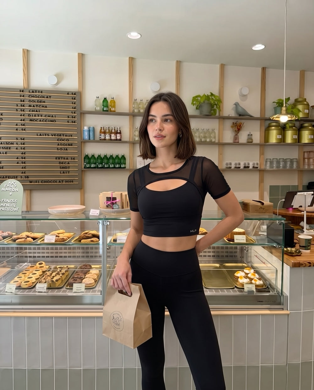 Woman in the black FitForm tee at a bakery counter with a paper bag