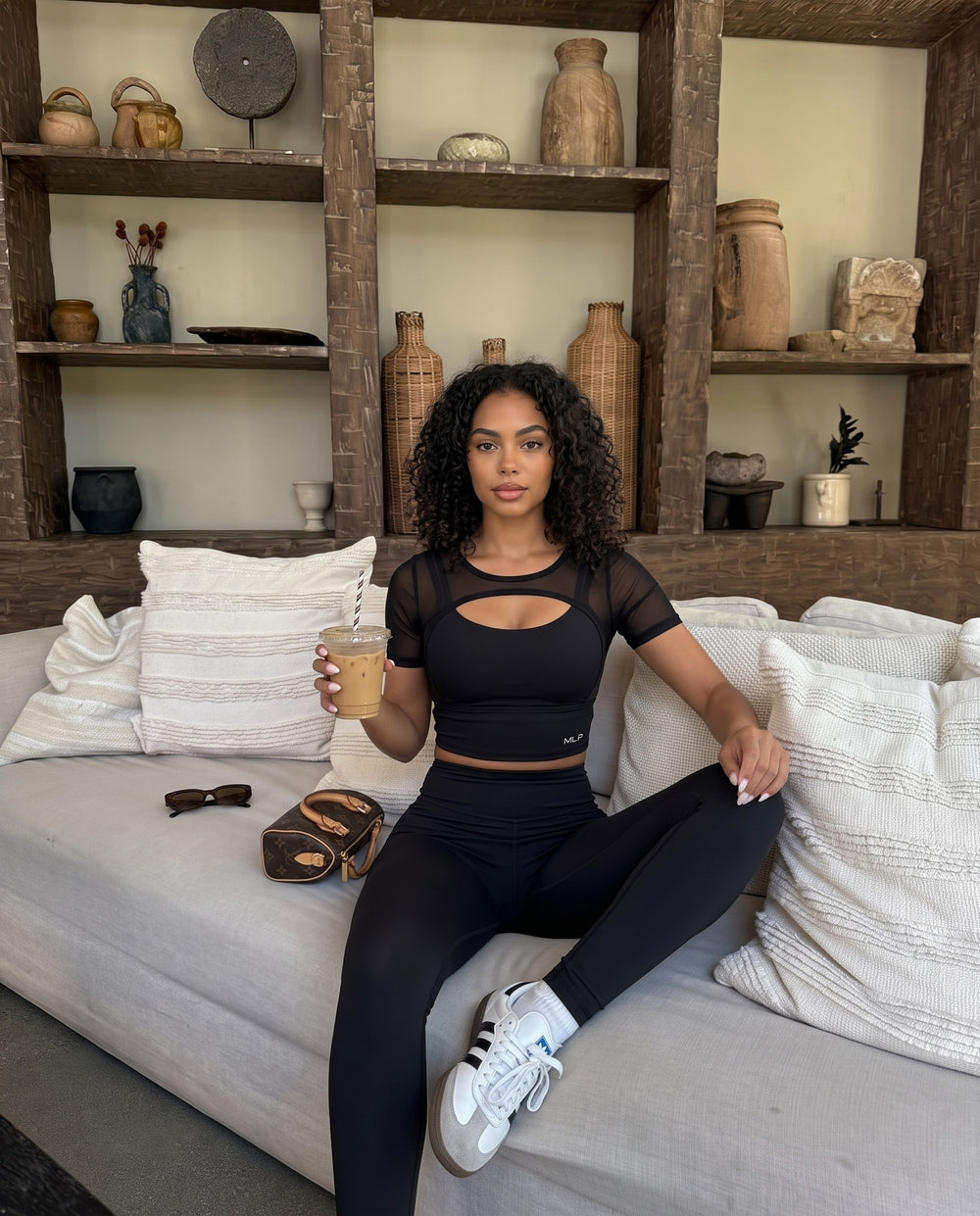 Woman in the black FitForm tee on the couch at home with an iced coffee